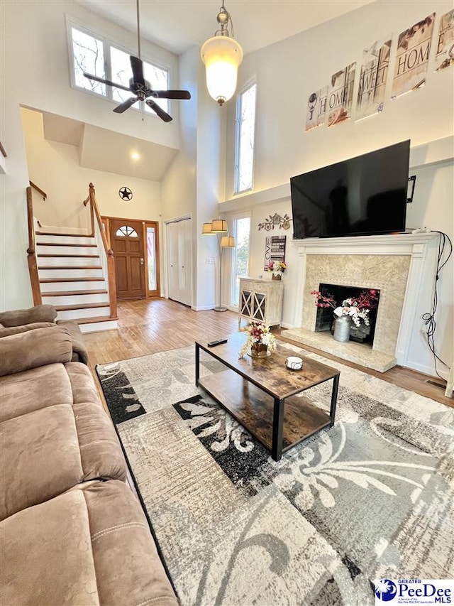 living room with stairway, a premium fireplace, a high ceiling, wood finished floors, and a ceiling fan