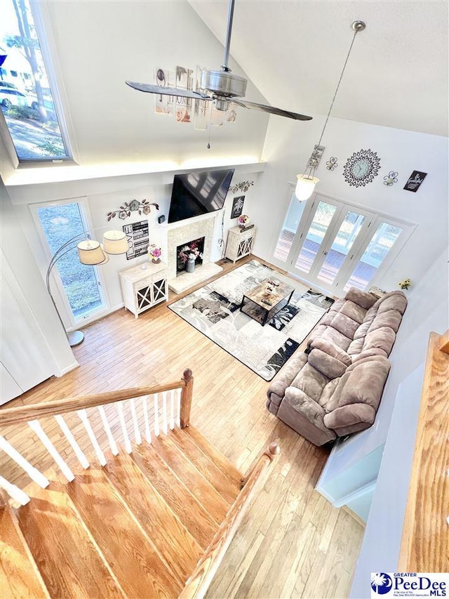 living room featuring wood finished floors, high vaulted ceiling, a fireplace with raised hearth, and ceiling fan