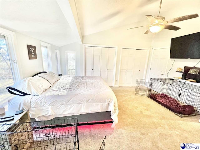 carpeted bedroom featuring two closets, ceiling fan, and vaulted ceiling