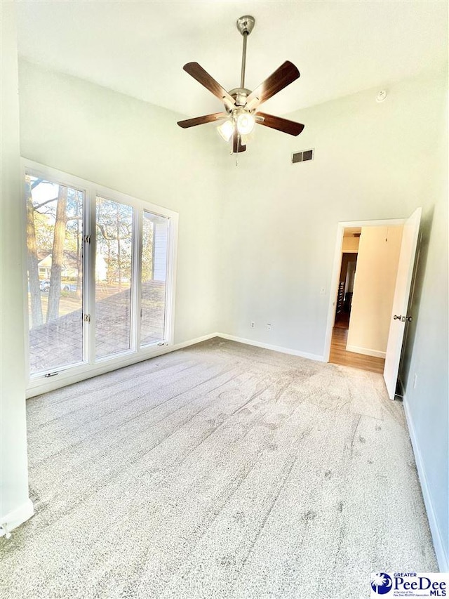 carpeted spare room with visible vents, ceiling fan, baseboards, and a towering ceiling