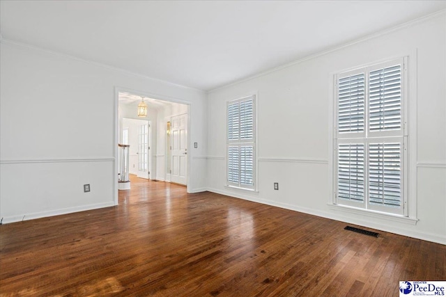 empty room with crown molding, wood finished floors, visible vents, and baseboards