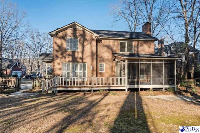 rear view of property with brick siding, a chimney, fence, and a sunroom