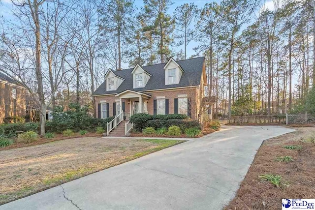 cape cod home with brick siding, a front lawn, and fence