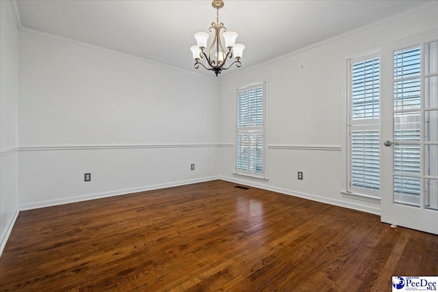 empty room with a notable chandelier, crown molding, visible vents, wood finished floors, and baseboards