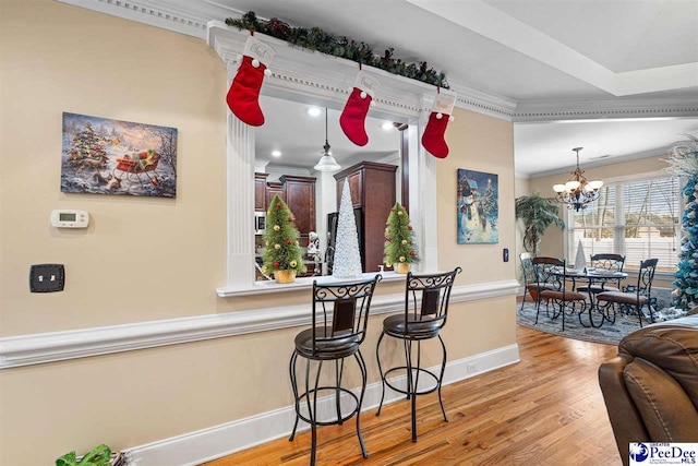 kitchen featuring decorative light fixtures, a notable chandelier, light hardwood / wood-style floors, crown molding, and a breakfast bar area