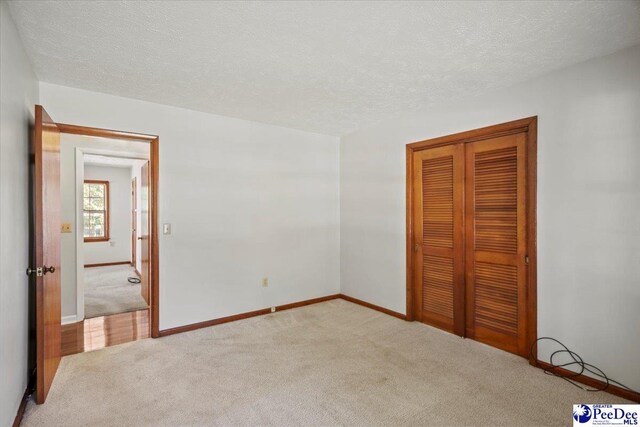 unfurnished bedroom with light colored carpet, a closet, and a textured ceiling