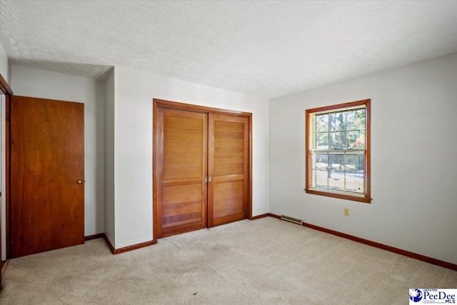 unfurnished bedroom featuring light colored carpet, a textured ceiling, and a closet