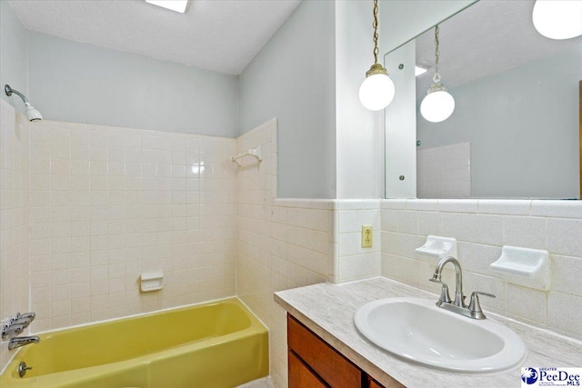 bathroom featuring tiled shower / bath, tile walls, vanity, and a textured ceiling