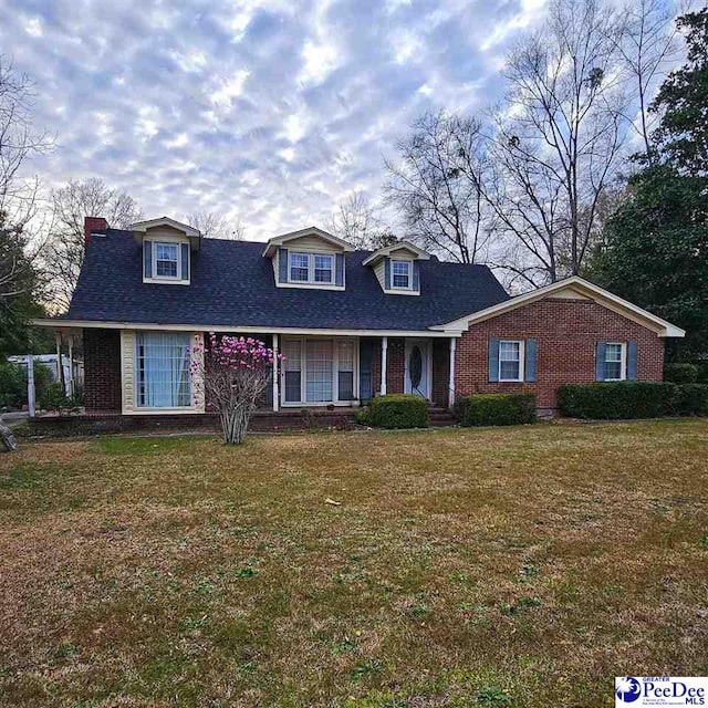 view of front facade with brick siding, a shingled roof, and a front lawn