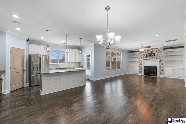 kitchen featuring stainless steel refrigerator with ice dispenser, hanging light fixtures, a kitchen island, a fireplace, and white cabinets
