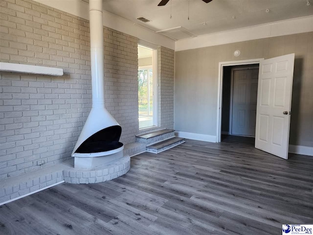 unfurnished living room featuring dark hardwood / wood-style flooring, brick wall, ceiling fan, and a wood stove