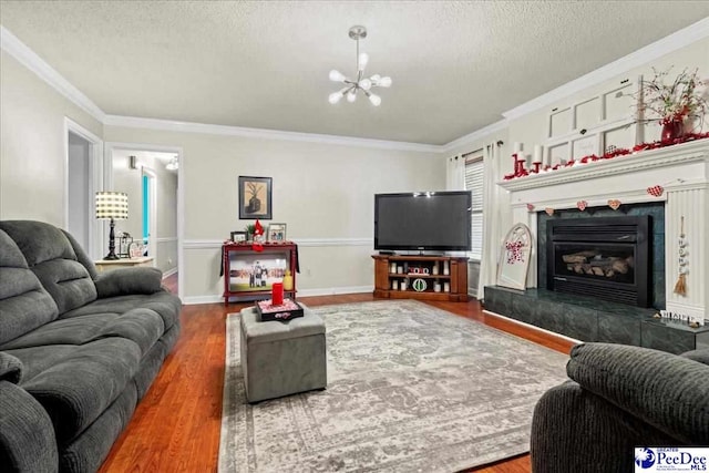 living room featuring crown molding, a tile fireplace, an inviting chandelier, wood-type flooring, and a textured ceiling