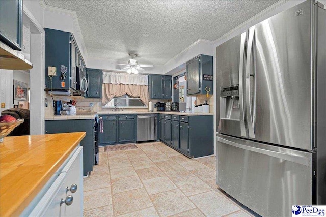 kitchen with blue cabinetry, ceiling fan, stainless steel appliances, ornamental molding, and a textured ceiling