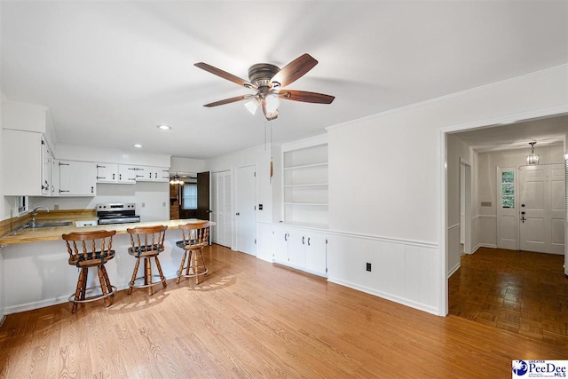 kitchen featuring a breakfast bar, sink, stainless steel electric range, kitchen peninsula, and white cabinets