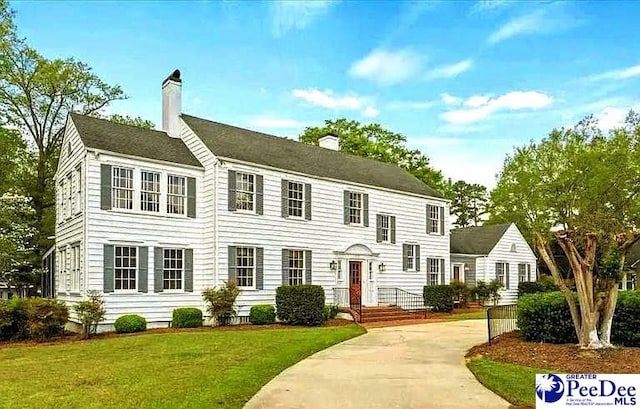 colonial inspired home featuring a chimney and a front yard