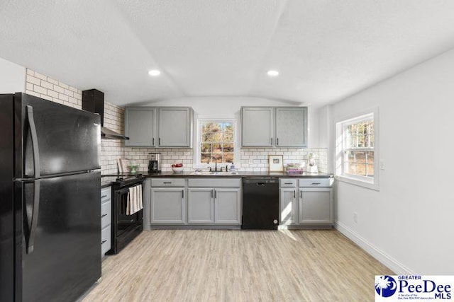 kitchen featuring dark countertops, wall chimney exhaust hood, gray cabinetry, and black appliances