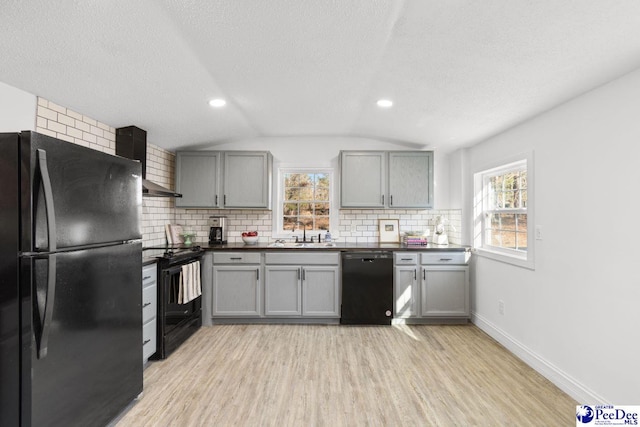 kitchen with dark countertops, black appliances, wall chimney exhaust hood, and gray cabinetry