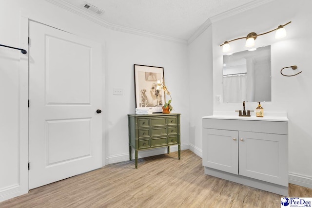 bathroom featuring baseboards, visible vents, ornamental molding, wood finished floors, and vanity