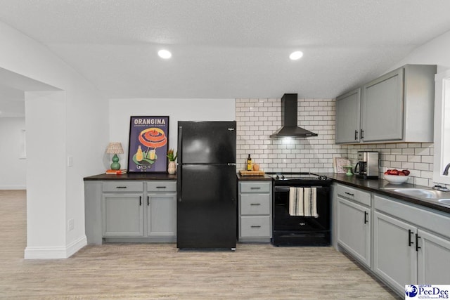 kitchen featuring light wood-style flooring, gray cabinetry, wall chimney exhaust hood, black appliances, and dark countertops