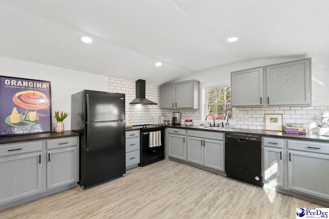 kitchen featuring black appliances, wall chimney range hood, dark countertops, and gray cabinetry