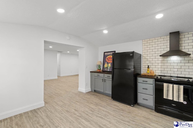 kitchen featuring gray cabinetry, light wood-style floors, vaulted ceiling, wall chimney range hood, and black appliances