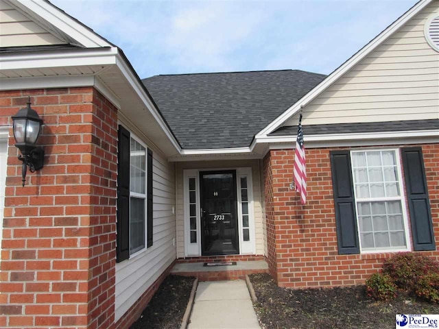 view of exterior entry featuring brick siding and a shingled roof