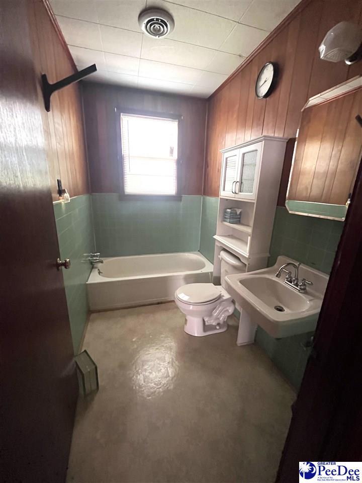 bathroom featuring a sink, toilet, visible vents, concrete floors, and wooden walls