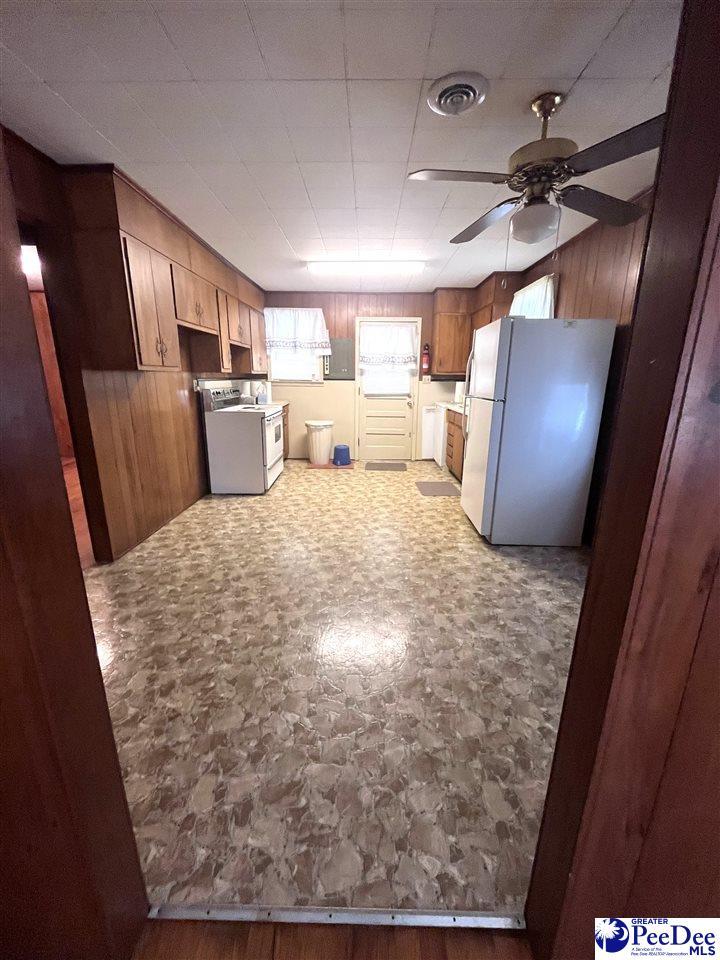 kitchen with a ceiling fan, visible vents, wooden walls, and white appliances