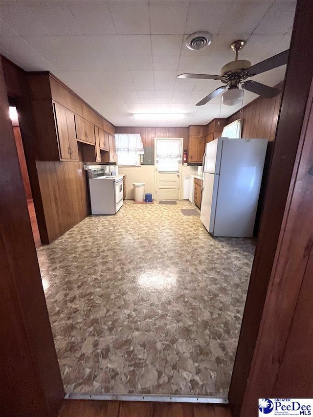 kitchen with a ceiling fan, visible vents, wooden walls, and white appliances