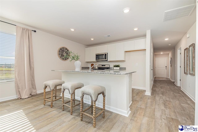 563 Strawberry Field Way, Galivants Ferry, SC 29544 - kitchen with stainless steel microwave, stove, light wood-style floors, white cabinetry, and light stone countertops