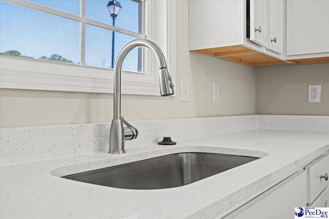 interior details featuring light stone counters, white cabinetry, and a sink