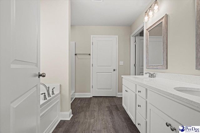 bathroom with a bath, double vanity, a sink, and wood finished floors