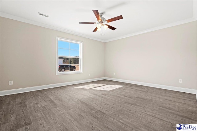 spare room with dark wood-style floors, visible vents, crown molding, and baseboards