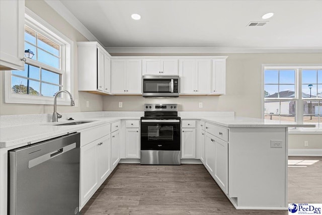 kitchen with stainless steel appliances, a peninsula, wood finished floors, a sink, and visible vents