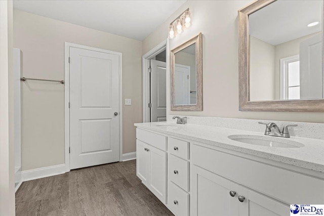 bathroom with double vanity, wood finished floors, a sink, and baseboards