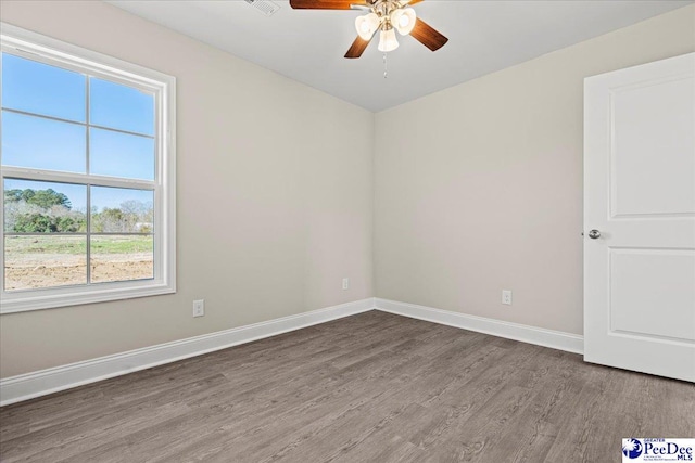 spare room with wood finished floors, a ceiling fan, and baseboards