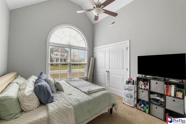 bedroom with carpet floors, a closet, ceiling fan, visible vents, and high vaulted ceiling
