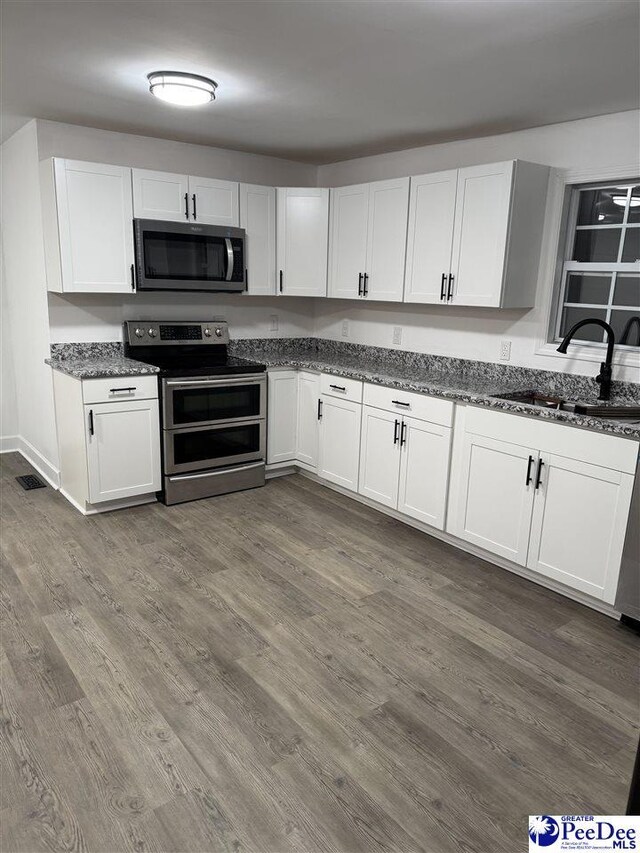 kitchen with sink, white cabinetry, dark stone countertops, dark hardwood / wood-style floors, and stainless steel appliances