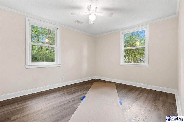 empty room with wood finished floors, plenty of natural light, baseboards, a textured ceiling, and crown molding
