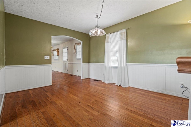 1101 E 3rd Ave, Lake View, SC 29563 - unfurnished dining area featuring arched walkways, hardwood / wood-style floors, a wainscoted wall, a textured ceiling, and a chandelier