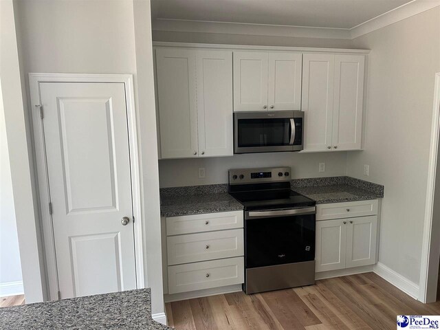 7845 E National Cemetery Rd, Florence, SC 29506 - kitchen with appliances with stainless steel finishes, light wood finished floors, white cabinetry, dark stone counters, and ornamental molding