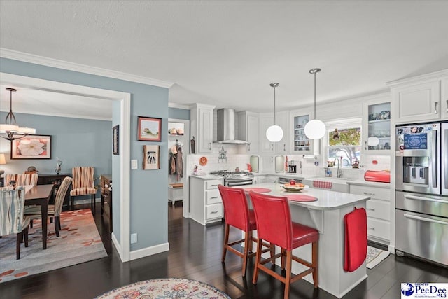 kitchen featuring stainless steel appliances, ornamental molding, decorative backsplash, wall chimney exhaust hood, and light countertops