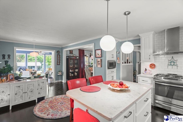 kitchen featuring crown molding, white cabinetry, wall chimney range hood, appliances with stainless steel finishes, and decorative backsplash