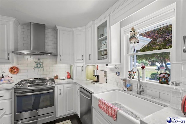 kitchen with white cabinets, wall chimney exhaust hood, stainless steel appliances, and a sink