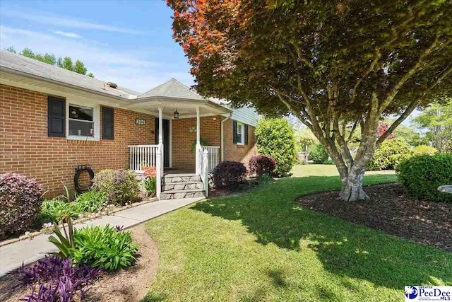 view of front of house with a porch, brick siding, and a front yard