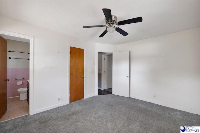 unfurnished bedroom with dark carpet, ceiling fan, and connected bathroom