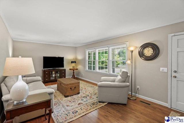 living area with baseboards, ornamental molding, wood finished floors, and visible vents