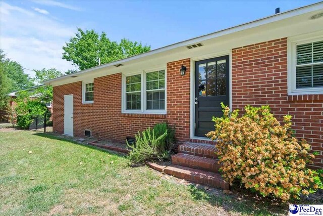 doorway to property with brick siding and a yard