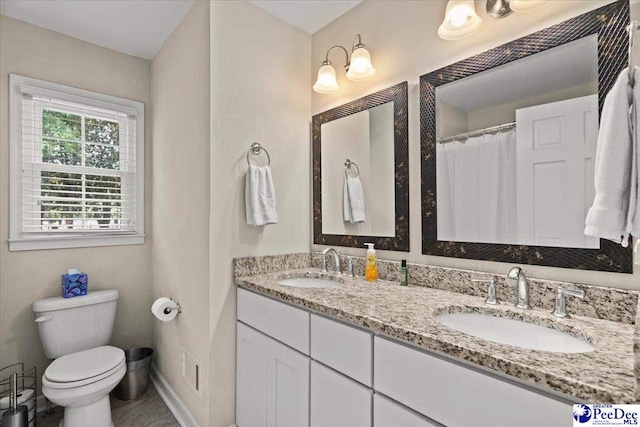 bathroom featuring double vanity, toilet, baseboards, and a sink