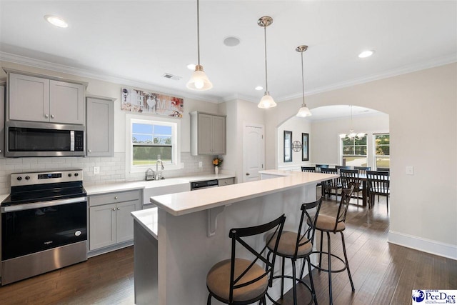 kitchen featuring pendant lighting, gray cabinets, a breakfast bar, appliances with stainless steel finishes, and a kitchen island